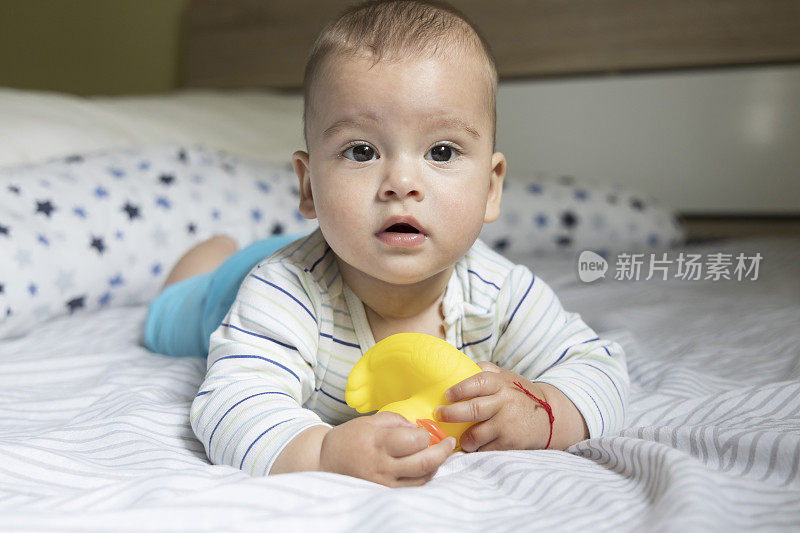 Little baby boy playing on the bed with a yellow duck on a rainy day